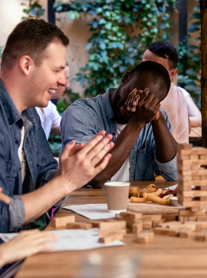 Een groep jonge volwassenen verzamelt zich rond een houten tafel om kleurrijke puzzelstukken in elkaar te zetten. Telefoons, mokken en snacks creëren een informele, sociale sfeer.